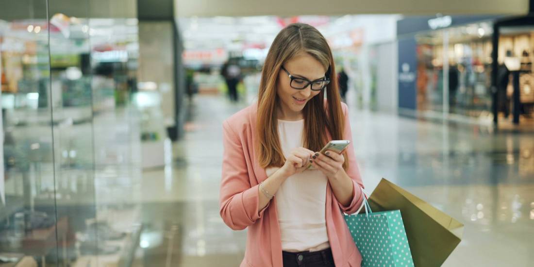 Shopper checking her phone in a mall, carrying shopping bags