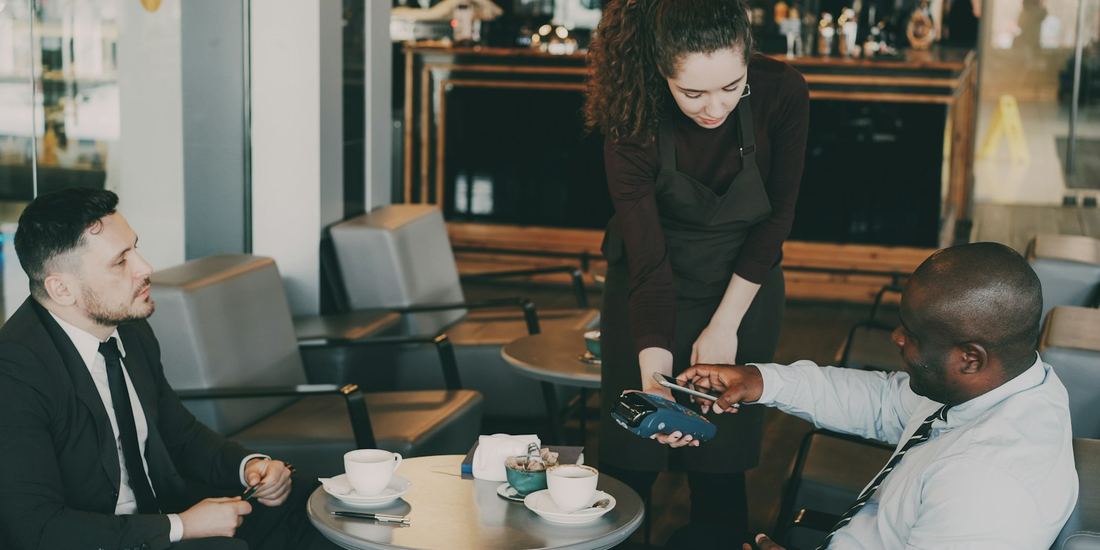 Customer paying with a phone at a cafe table while a colleague looks on